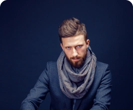 Egy szakállas férfi öltönyben és sállal pókerzsetonokat gyűjt egy asztalnál, amelyen kártyák és egy whiskys pohár található. A hangulat feszült és koncentrált