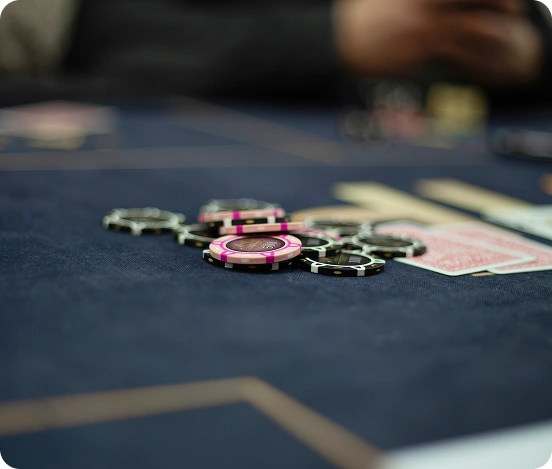 Pókerszoba jelenet, amelynek középpontjában a sötétkék filcfelületen szétszórt pókerzsetonok és kártyák állnak, feszült, versenyszerű hangulatot árasztva